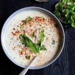 creamy onion raita in a grey ceramic bowl topped with mint leaves, extra onions in the side in small metal plate