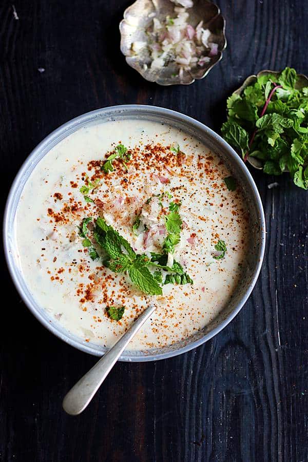 creamy onion raita in a grey ceramic bowl topped with mint leaves, extra onions in the side in small metal plate