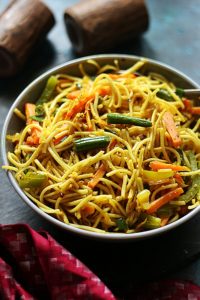 vegetarian hakka noodles served in a grey ceramic bowl with salt and pepper shakers in the background.