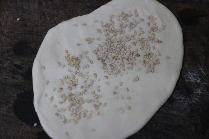 kulcha dough rolled into oval disc and topped with sesame seeds