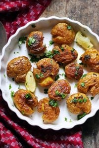 crispy smashed potatoes served in a ceramic plate with lemon wedges.