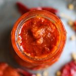homemade best harissa sauce in a glass jar placed on a copper plate.