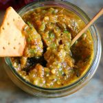 a jar of roasted tomato salsa with a nachos chip dipped in it.