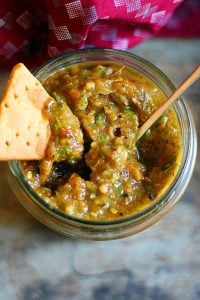 a jar of roasted tomato salsa with a nachos chip dipped in it.