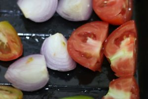 cut tomatoes and onions placed on a greased bakig sheet.