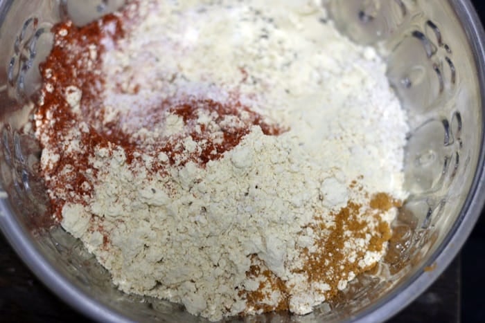 chili powder, turmeric powder, sesame seeds, carom seeds, cumin seeds, oil, salt, baking soda and sugar added to chickpea flour for making crackers
