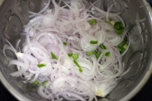 Sliced onions and finely chopped green chilies in a large bowl