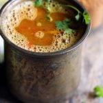 frothy homemade tomato rasam in a tall brass vessel
