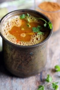 frothy homemade tomato rasam in a tall brass vessel