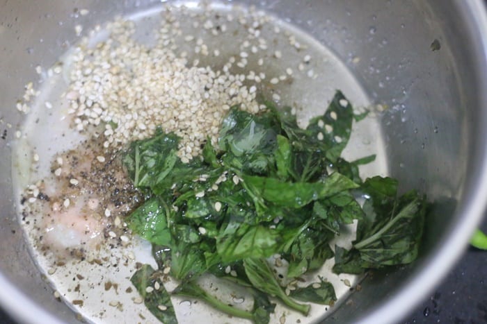dressing ingredients for tomato salad- vinegar, olive oil, sugar, salt, pepper, sesame seeds and basil leaves in a bowl