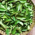 Fresh curry leaves in a brass bowl.