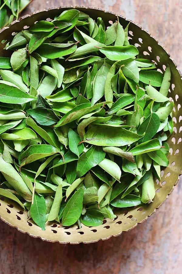Fresh curry leaves in a brass bowl.