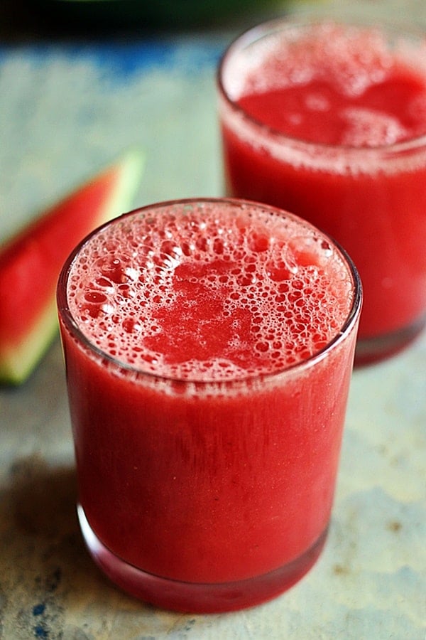 Chilled refreshing watermelon juice served in a glass with some fresh watermelon in the background